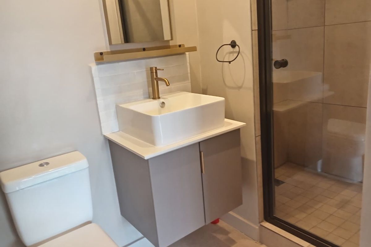 Modern bathroom featuring a vessel sink with brass faucet, vanity cabinet, toilet, and a glass-enclosed shower with tiled finishes.