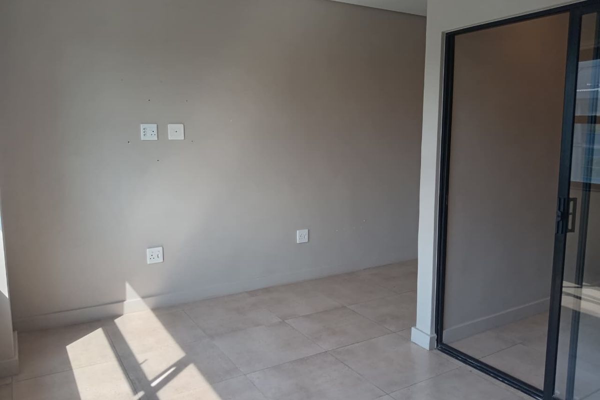 A bright, empty living area featuring neutral tiled flooring and a modern sliding glass door leading to an outdoor space.
