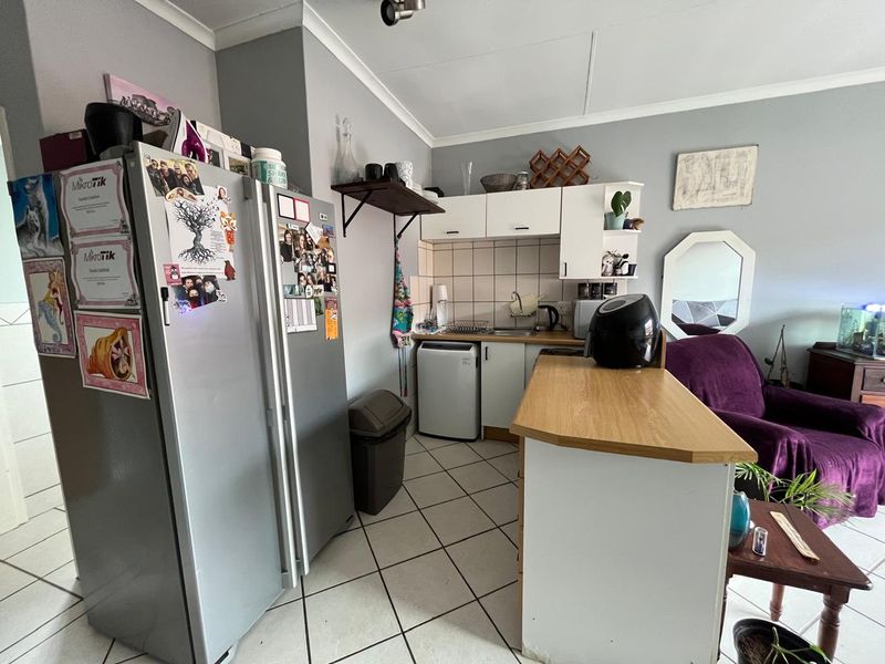 Compact open-plan kitchen area featuring tiled flooring, built-in cabinetry, a tiled backsplash, and a functional breakfast counter.