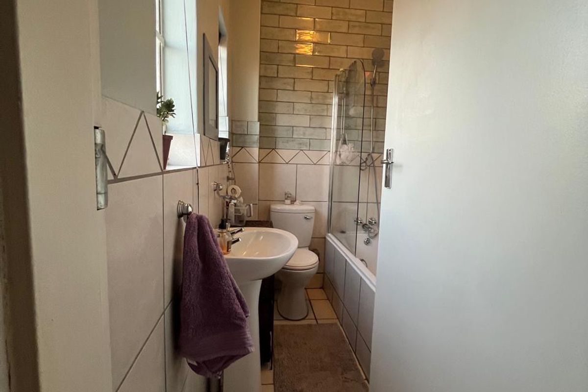 A functional bathroom featuring a pedestal basin, toilet, and a bathtub with a shower screen, finished with neutral wall and floor tiling.