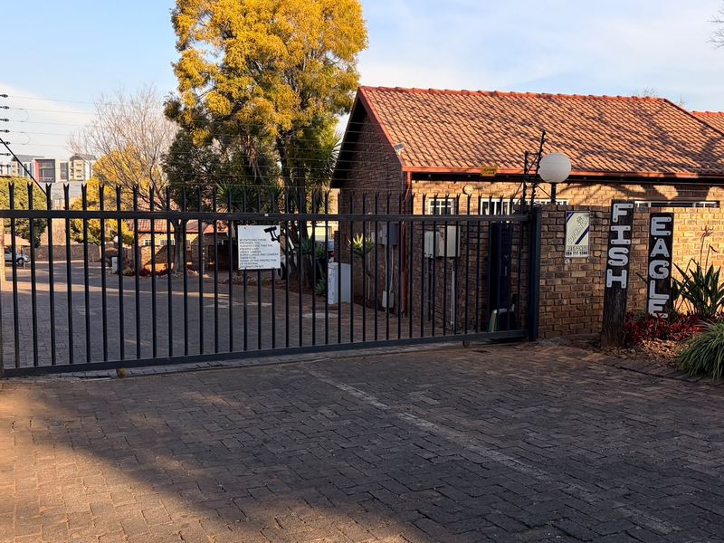 Front entrance view of the property featuring a secure metal gate, brick boundary wall, electric fencing, and a paved driveway.