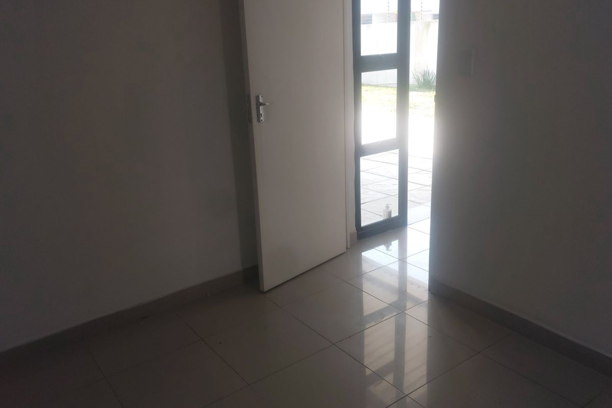 An empty interior entry space featuring tiled flooring and an aluminium framed glass door leading to an outdoor area.
