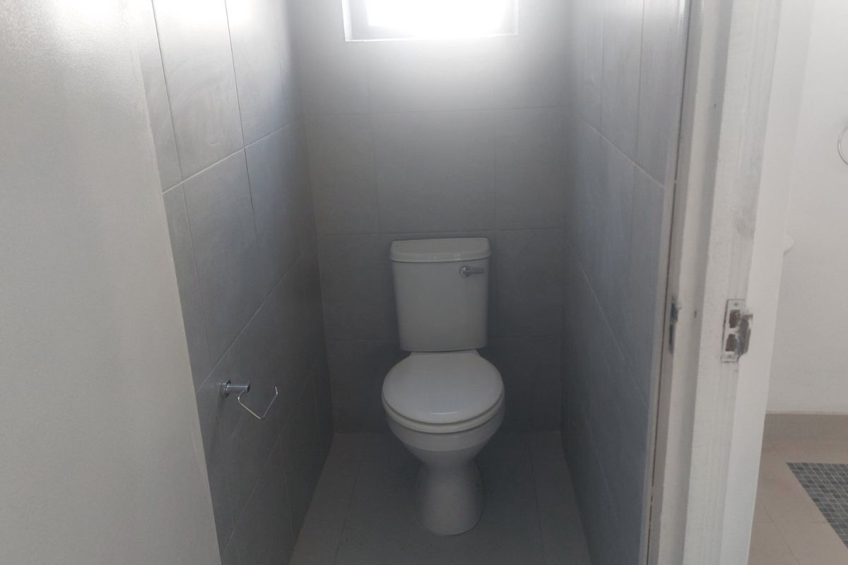 A compact, neutral-toned bathroom featuring tiled walls and flooring, equipped with a standard toilet and essential fixtures.