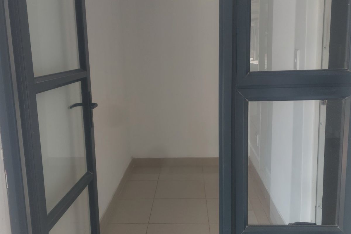 A clean, empty entrance area featuring modern dark-framed glass doors and neutral tiled flooring, providing a bright and welcoming transition space.