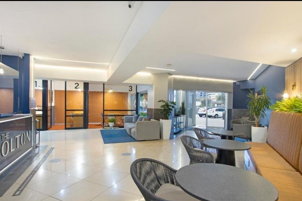 Modern apartment complex clubhouse featuring a reception area, glass-partitioned meeting rooms, tiled flooring, and comfortable built-in seating arrangements.