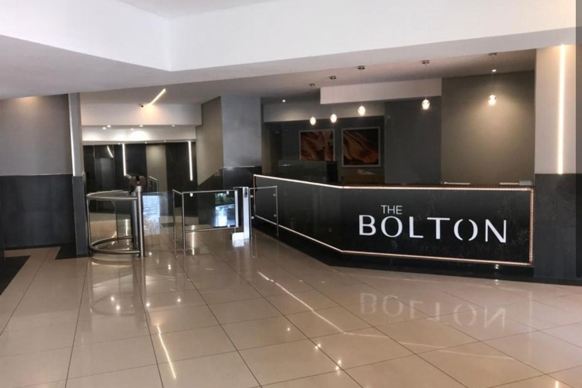 Modern apartment building lobby featuring a professional reception desk, secure turnstile access, and polished tiled flooring with contemporary lighting.