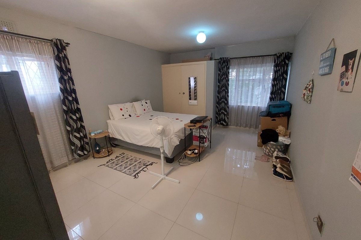Spacious bedroom featuring neutral tiled flooring and a built-in wardrobe, offering a functional layout with ample natural light.
