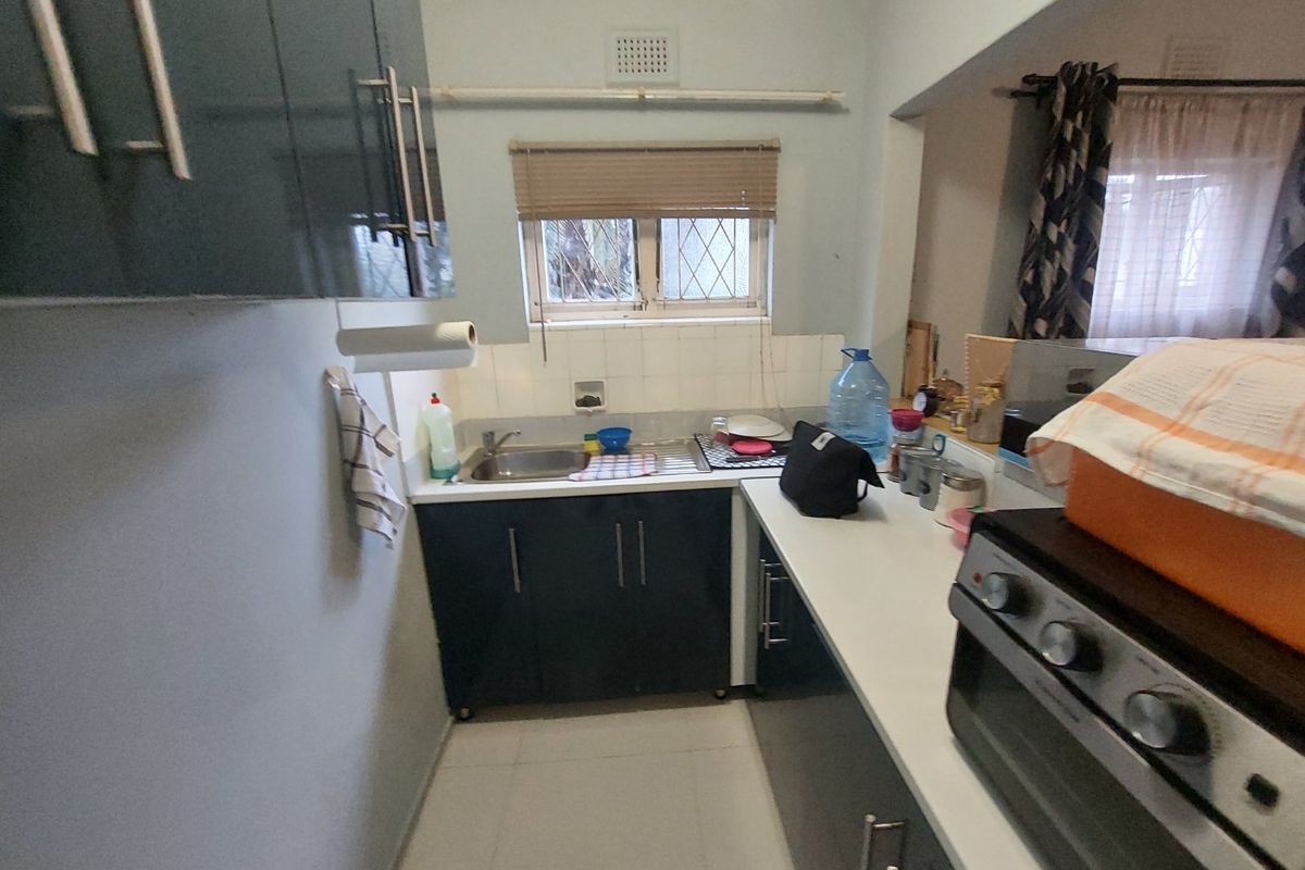 A compact kitchen featuring dark built-in cabinetry, a stainless steel sink, tiled backsplash, and tiled flooring with a window providing natural light.