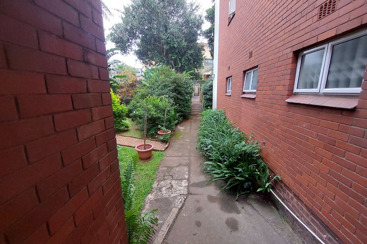 A side pathway leading to a rear garden area, featuring red brick exterior walls and established landscaping.
