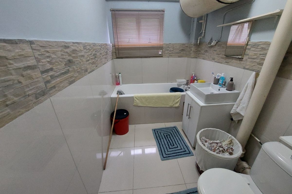 A functional bathroom featuring a bathtub, vanity basin, toilet, and tiled finishes, with an exposed water heater unit.
