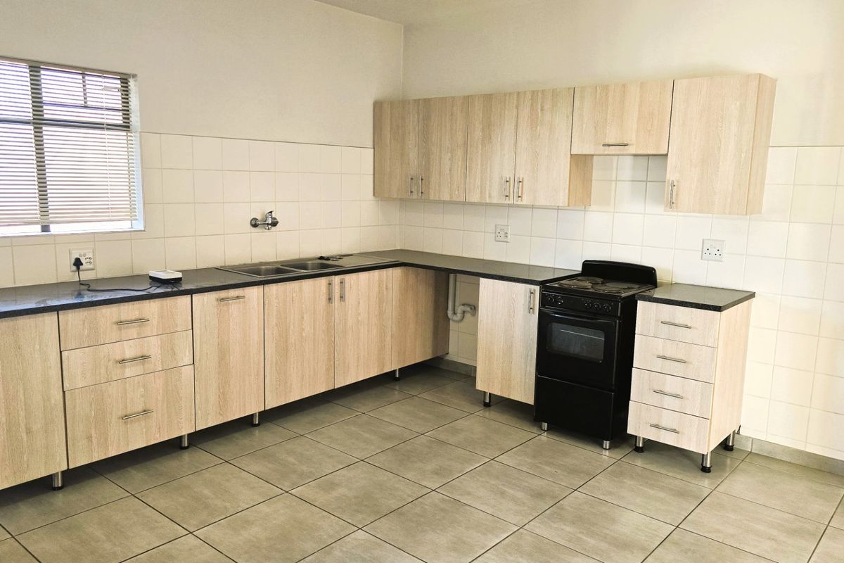 A clean, functional kitchen featuring light wood-look cabinetry, dark countertops, a double sink, and a freestanding stove with tiled splashbacks.