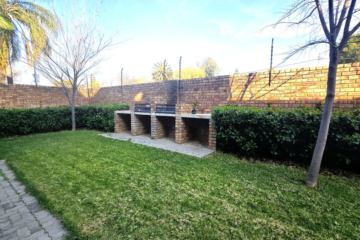 Private rear garden featuring a built-in brick braai area, established lawn, paved walkway, and secure brick boundary wall with electric fencing.