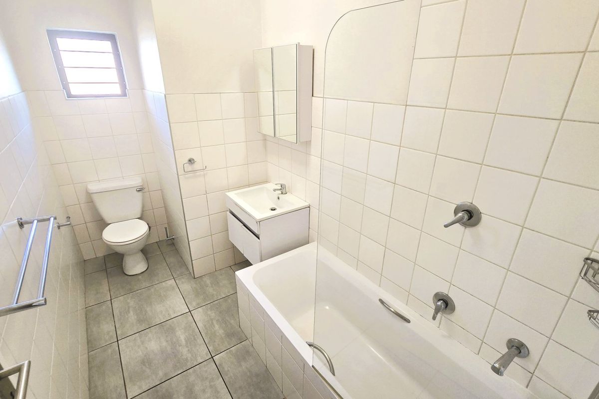 A clean, functional bathroom featuring a bathtub with a glass screen, a modern vanity unit, and neutral tiled finishes throughout.