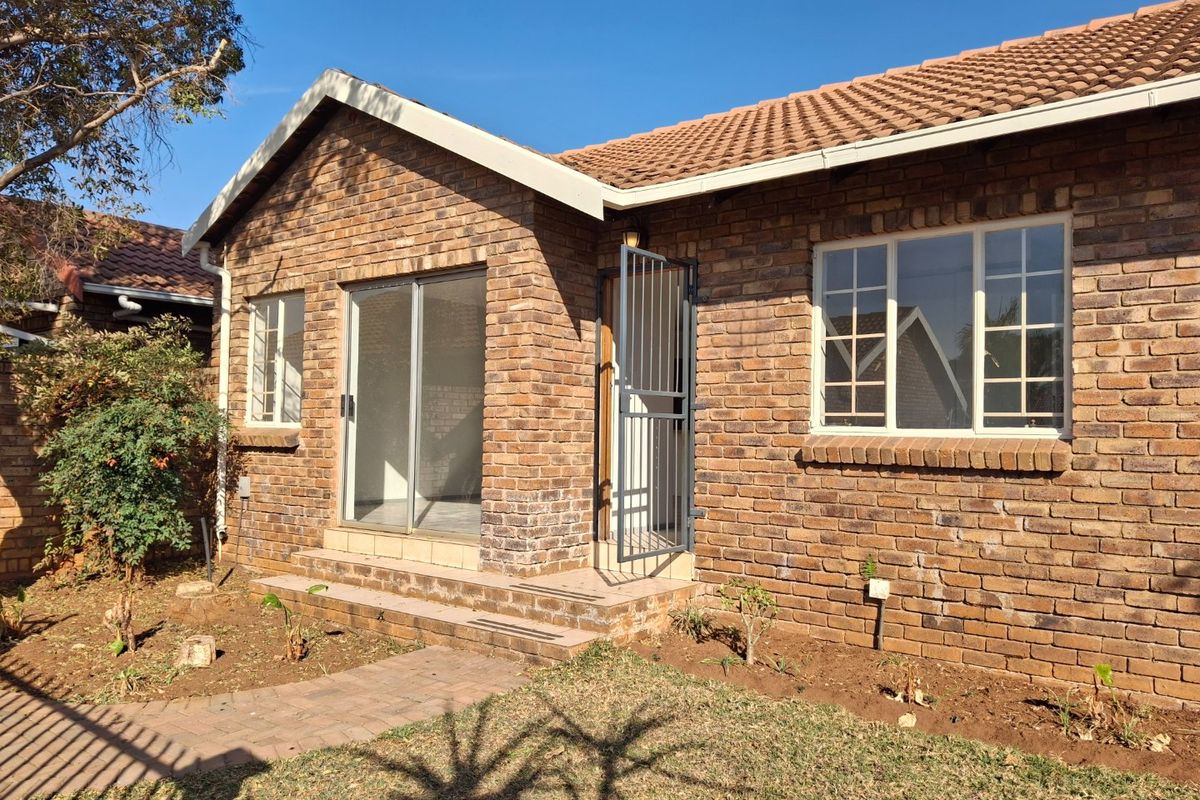 Rear view of a face brick townhouse featuring a sliding glass door, security gate, and a small garden area with a paved walkway.
