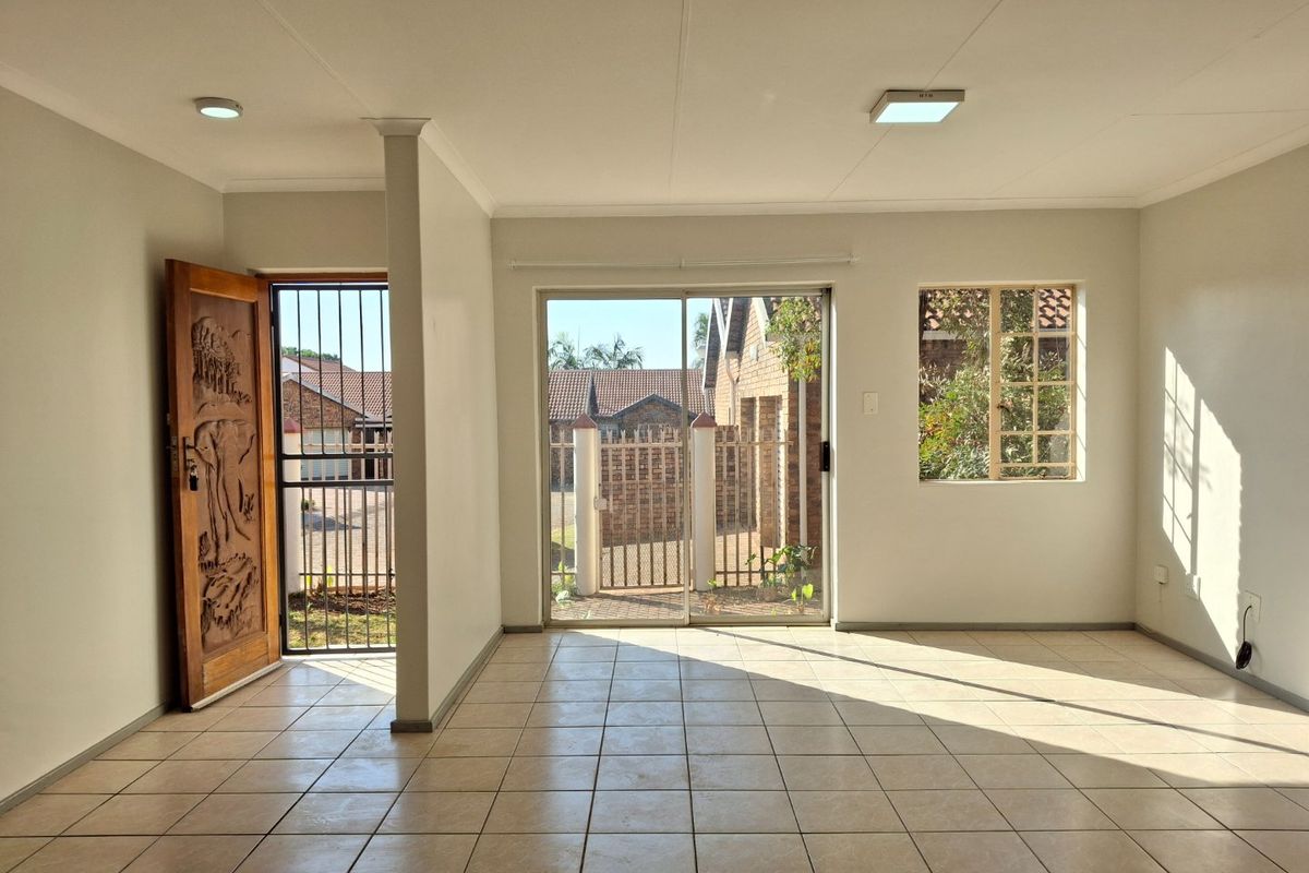 A bright, empty living area featuring tiled flooring, a decorative wooden entrance door, and sliding glass doors leading to the exterior.
