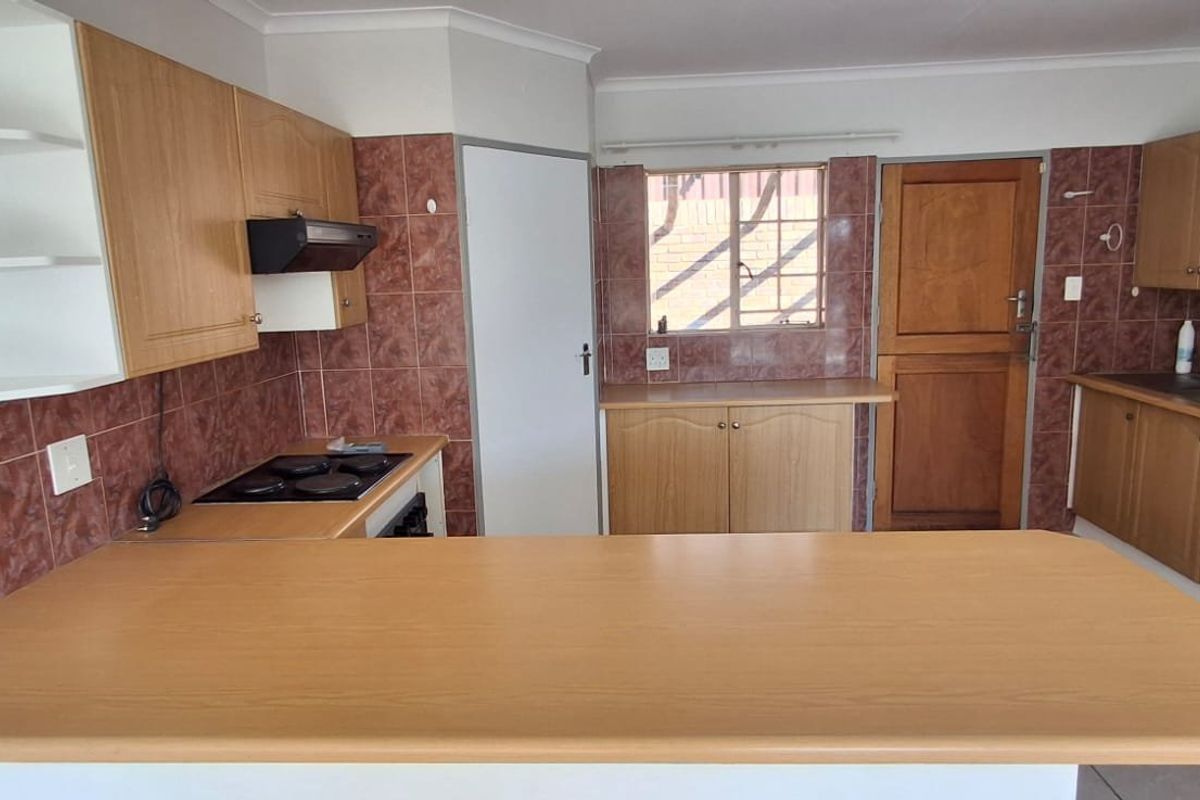 A functional kitchen featuring laminate countertops, built-in wooden cabinetry, an electric hob with extractor, and a double bowl sink with tiled splashbacks.