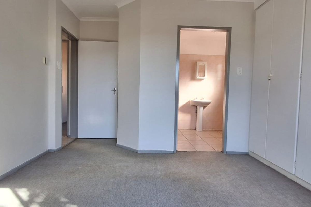 A vacant bedroom featuring built-in cupboards, carpeted flooring, and direct access to an en-suite bathroom.