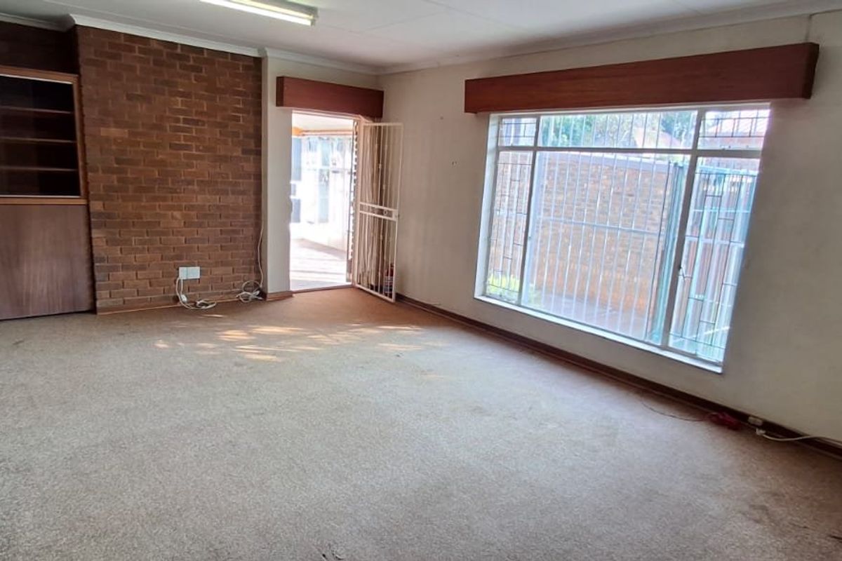 Spacious living room featuring a brick accent wall, built-in cabinetry, and large windows with security bars, offering a blank canvas for renovation.