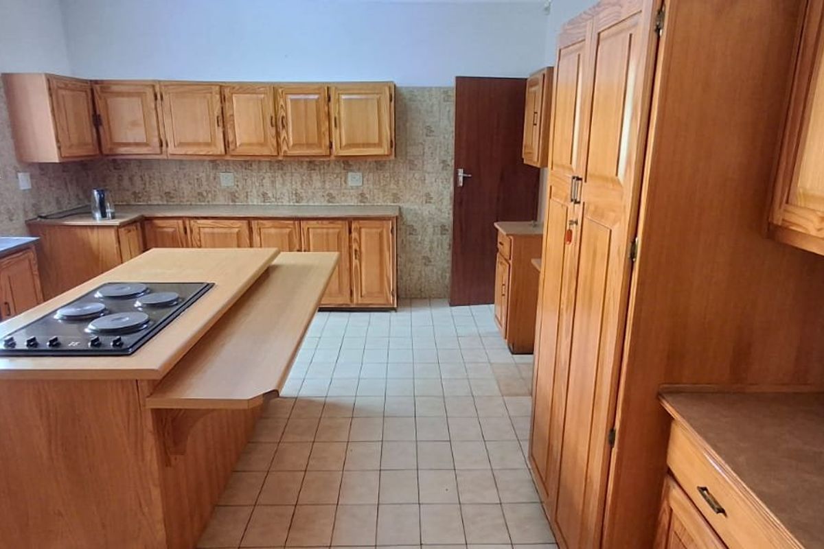 Spacious kitchen featuring extensive wooden cabinetry, a central island with a built-in electric hob, double sink, and tiled flooring throughout.