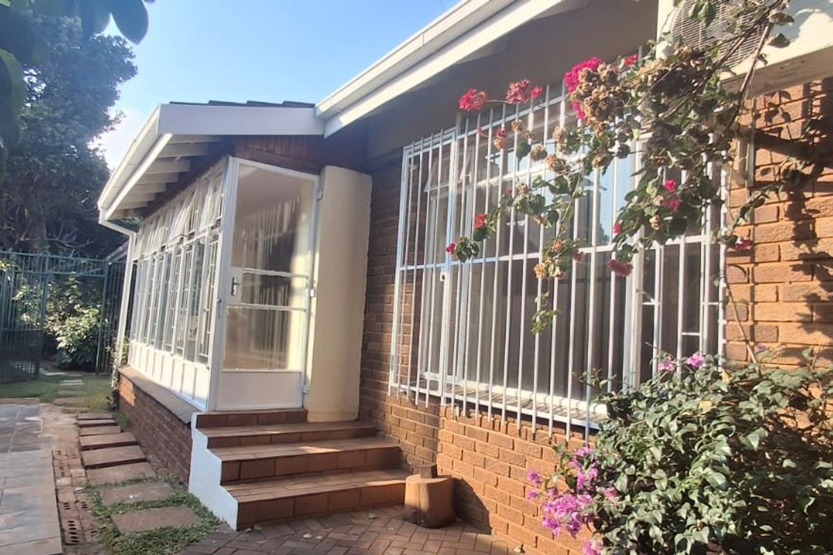 Rear exterior view of the house featuring a brick facade, security bars on windows, an enclosed sunroom, and a paved patio area.