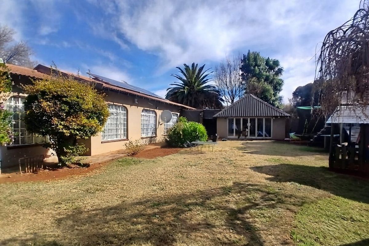 Rear view of the property featuring a spacious garden, tiled roof with solar panels, and sliding glass doors leading to the main dwelling.
