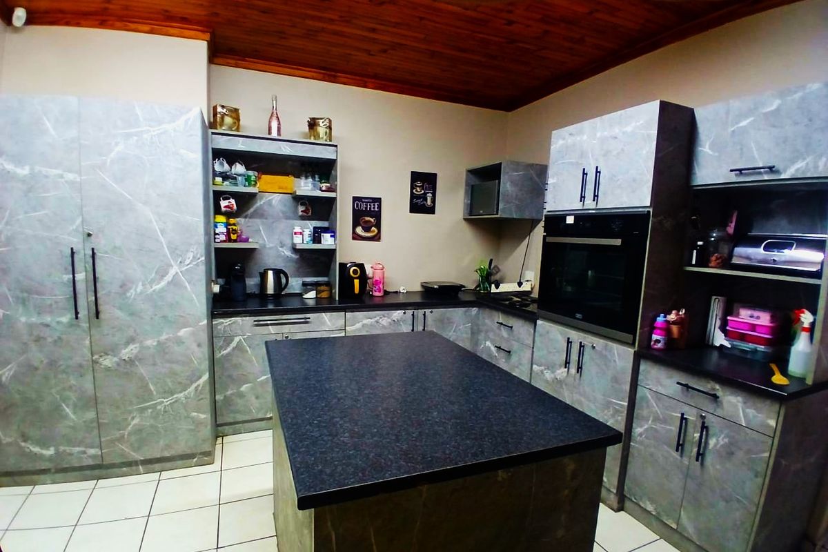 Modern kitchen featuring marble-effect cabinetry, a central island, built-in oven, and a distinctive timber ceiling with tiled flooring.
