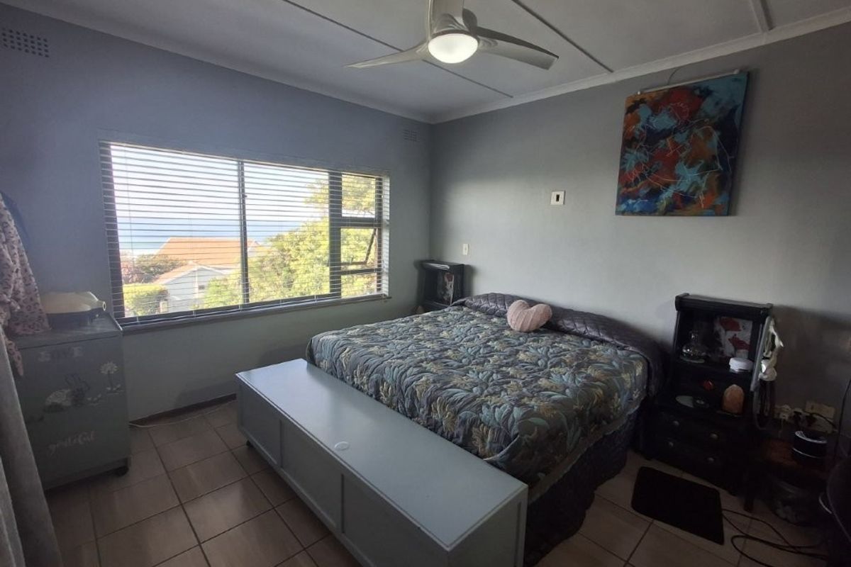 A bedroom featuring tiled flooring, a ceiling fan, and a large window providing natural light and a view of the surrounding area.
