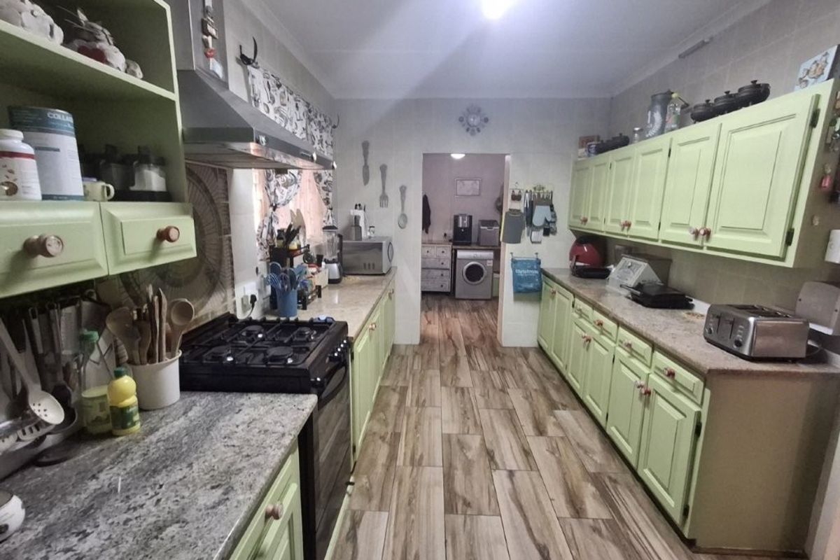 A functional kitchen featuring light green cabinetry, stone countertops, gas stove with extractor fan, and wood-look laminate flooring, with an adjacent laundry area.