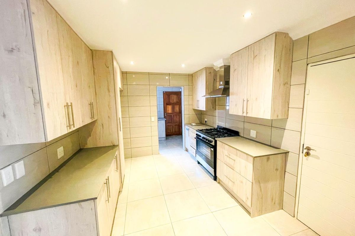A modern, well-lit kitchen featuring light wood-finish cabinetry, tiled walls and flooring, and a built-in gas stove with an extractor fan.