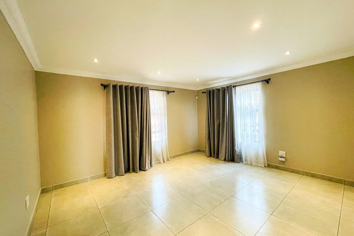 A bright, empty living room featuring neutral tiled flooring, recessed downlighting, and coved cornicing, providing a clean and versatile space.