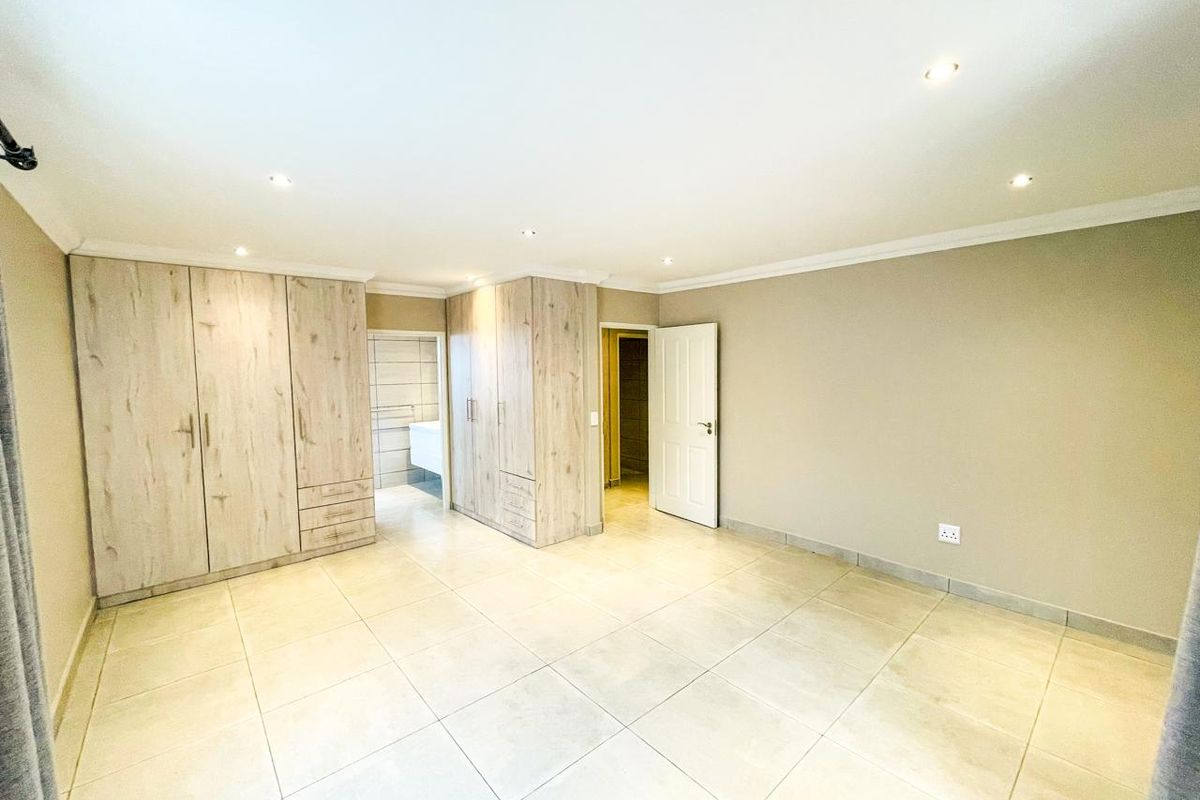 Spacious bedroom featuring neutral tiled flooring, recessed downlighting, and extensive built-in cabinetry with direct access to an en-suite bathroom.