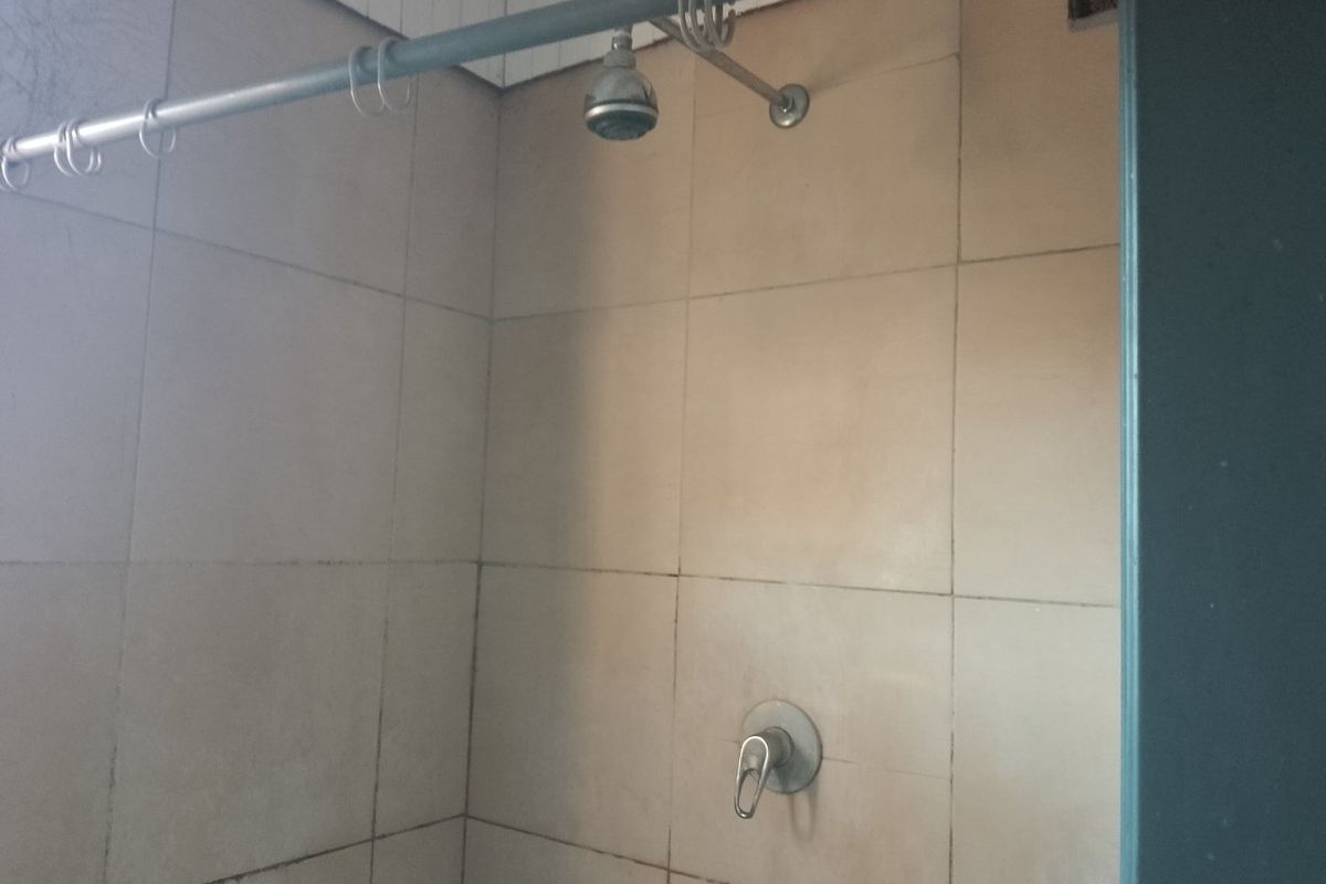 A functional shower area featuring tiled walls, a standard shower head, and mixer tap, currently showing signs of wear and dated finishes.
