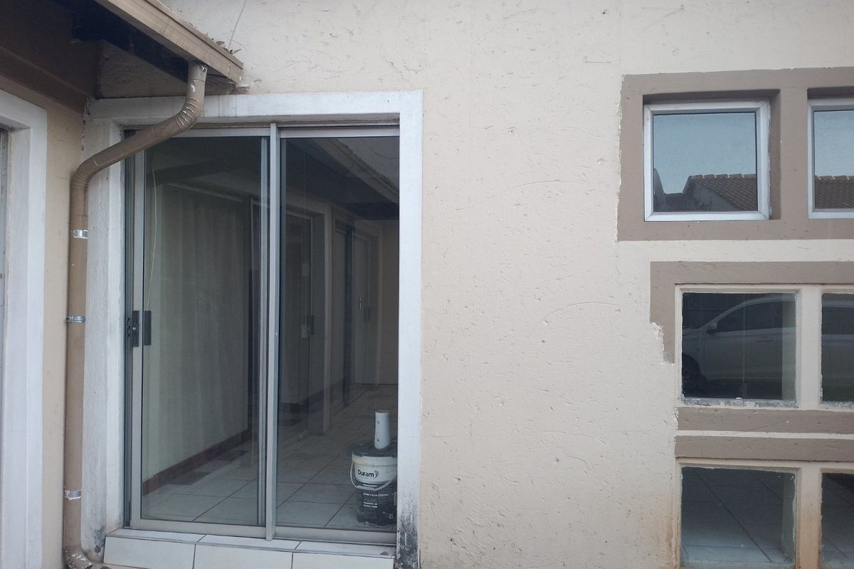Exterior view of the rear facade featuring a sliding glass door, aluminium window frames, and tiled flooring with visible signs of wear.