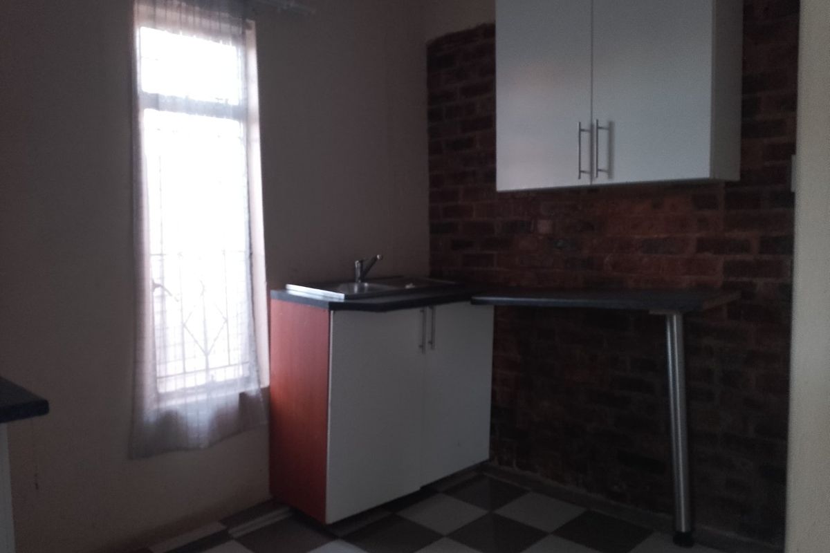 A compact kitchen area featuring white cabinetry, a sink, and an exposed brick feature wall with checkered floor tiles.