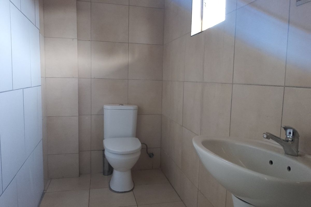 A functional bathroom featuring neutral ceramic wall and floor tiles, a pedestal washbasin with chrome mixer tap, and a standard close-coupled toilet.