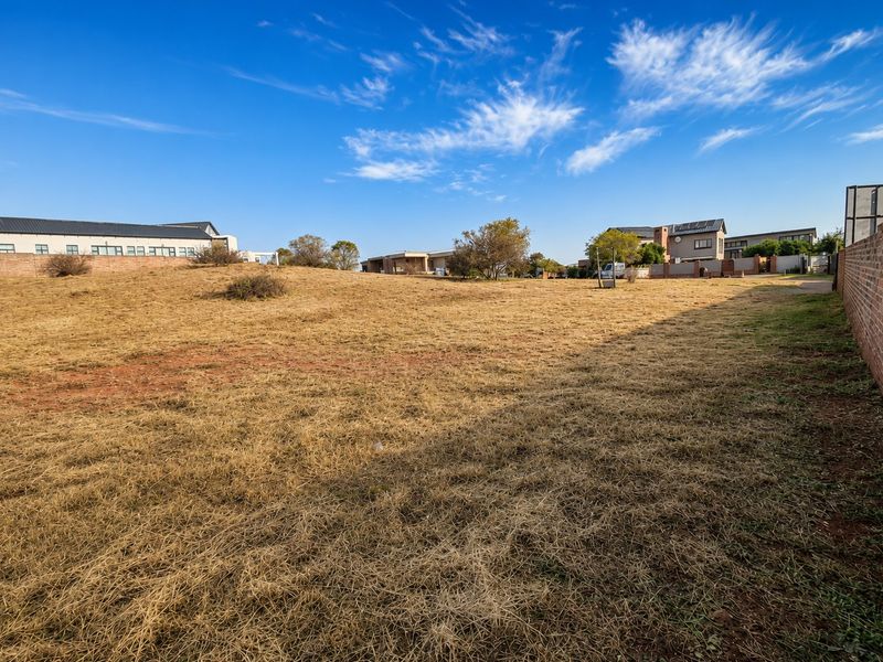 A vacant residential plot featuring dry grass and a brick boundary wall, situated within a developed neighborhood.