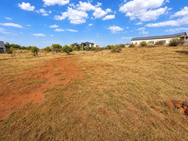 A view of an undeveloped residential plot featuring natural dry grass and surrounding neighborhood homes in the distance.