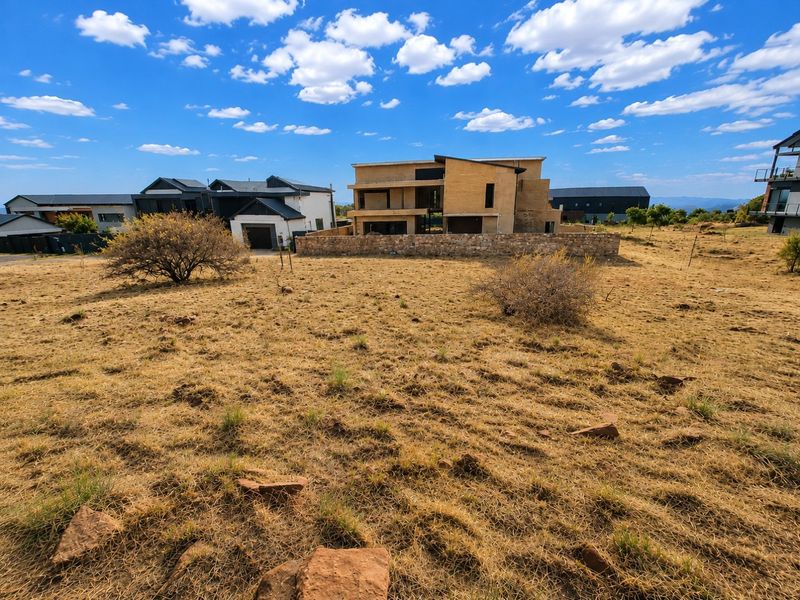 A view of a residential plot featuring a partially constructed multi-level home with a stone boundary wall in a developing estate.