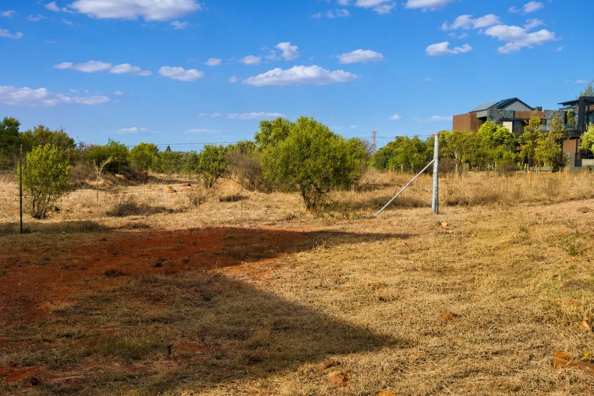 A view of a vacant residential plot featuring dry grass, native shrubs, and perimeter wire fencing with metal posts.