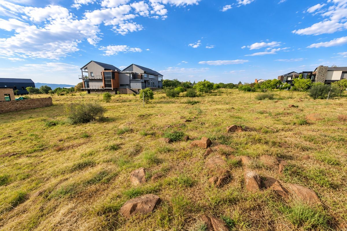 A view of a vacant residential plot featuring natural rocky terrain and native vegetation, with neighboring modern homes visible in the background.