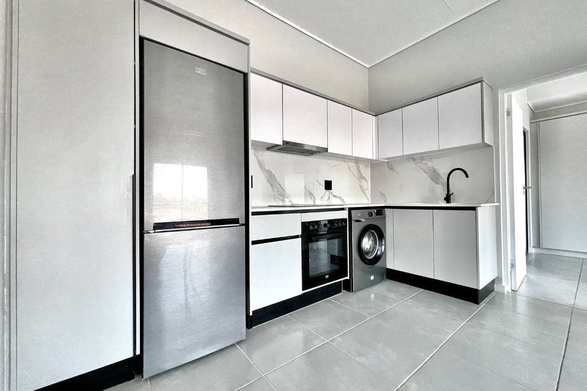 Modern kitchen featuring sleek white cabinetry, marble-look splashback, integrated oven, extractor fan, and high-quality tiled flooring.
