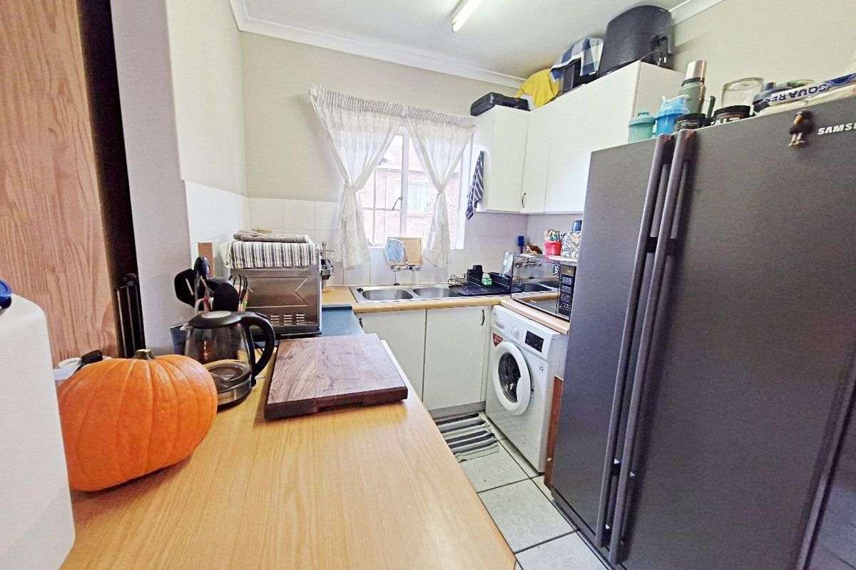 Compact kitchen featuring laminate countertops, double sink, tiled flooring, and built-in cabinetry with an integrated washing machine.