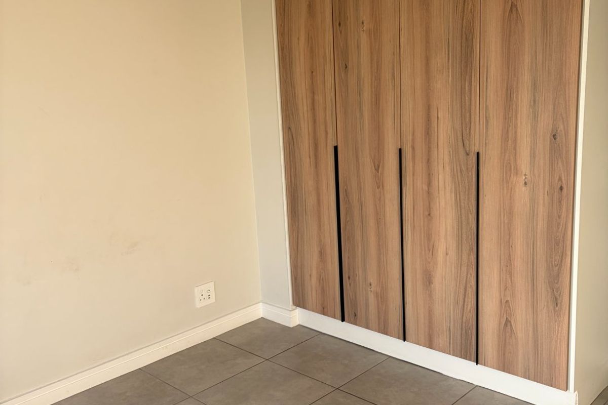 An empty bedroom featuring modern wood-finish built-in wardrobes and neutral grey floor tiles.