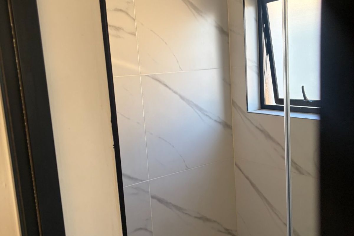 A modern, clean shower area featuring contemporary marble-look wall tiles, neutral floor tiling, and a functional casement window for natural light and ventilation.
