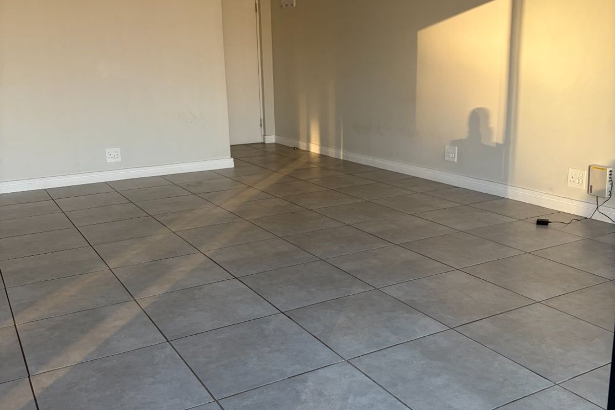 An empty, sunlit living area featuring neutral walls and grey tiled flooring, providing a blank canvas for interior design.