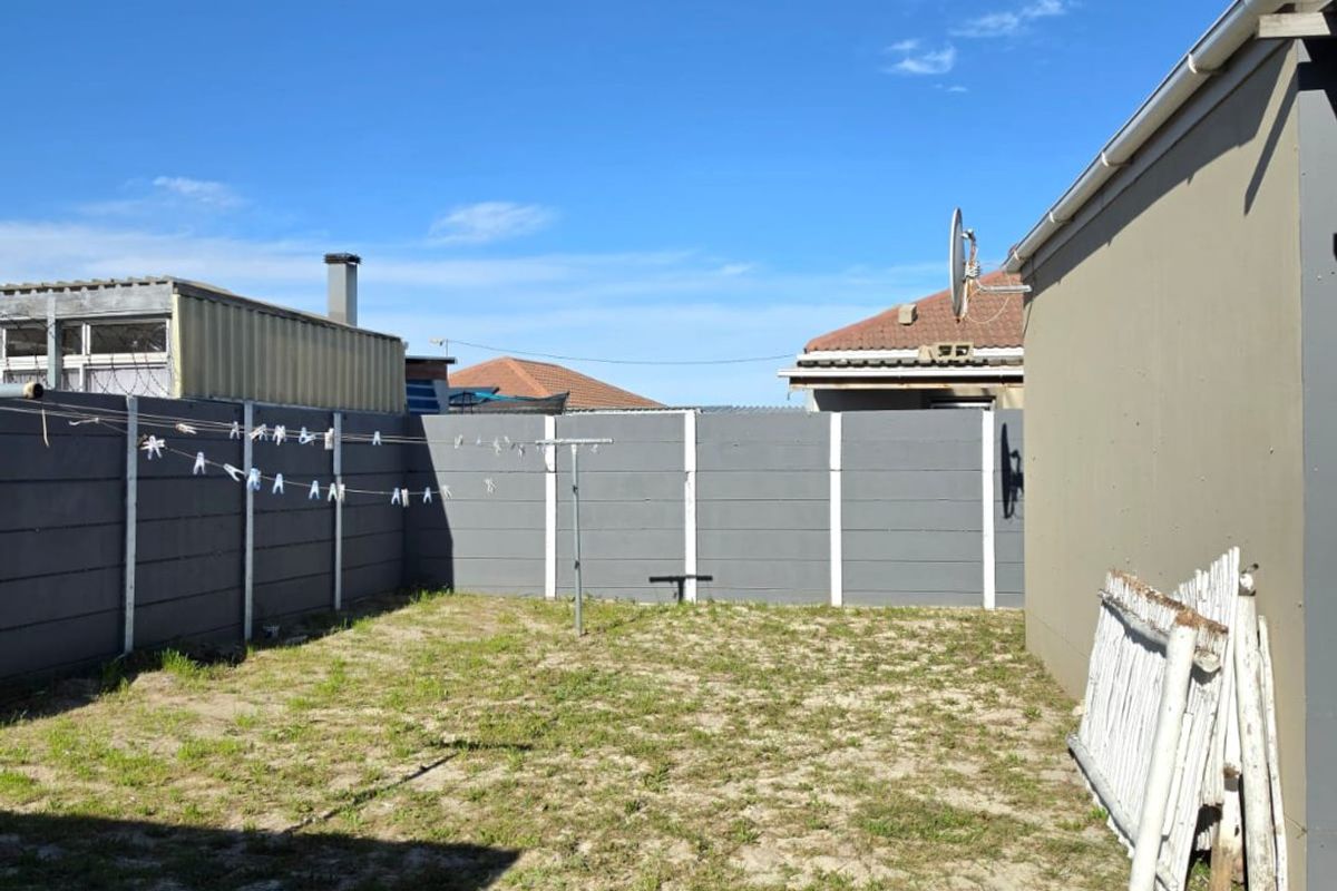 A rear garden area featuring a precast concrete boundary wall and a side elevation of the house with guttering.