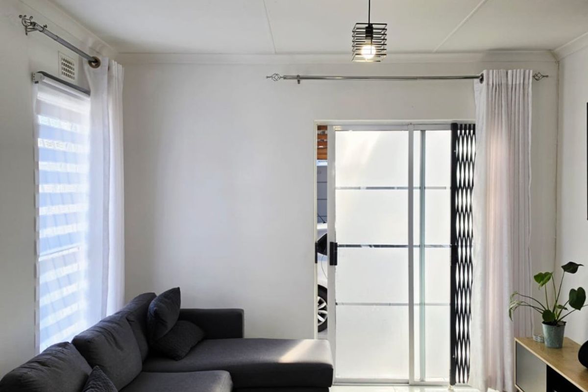 A bright living room featuring tiled flooring, a modern pendant light, and a sliding glass door with an integrated security gate.