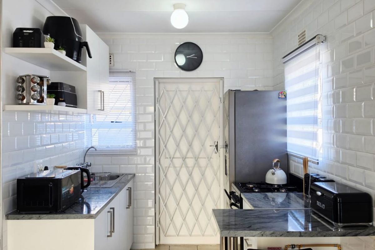 A compact, well-maintained kitchen featuring white subway tile walls, granite countertops, a gas hob, and a secure rear entrance door.