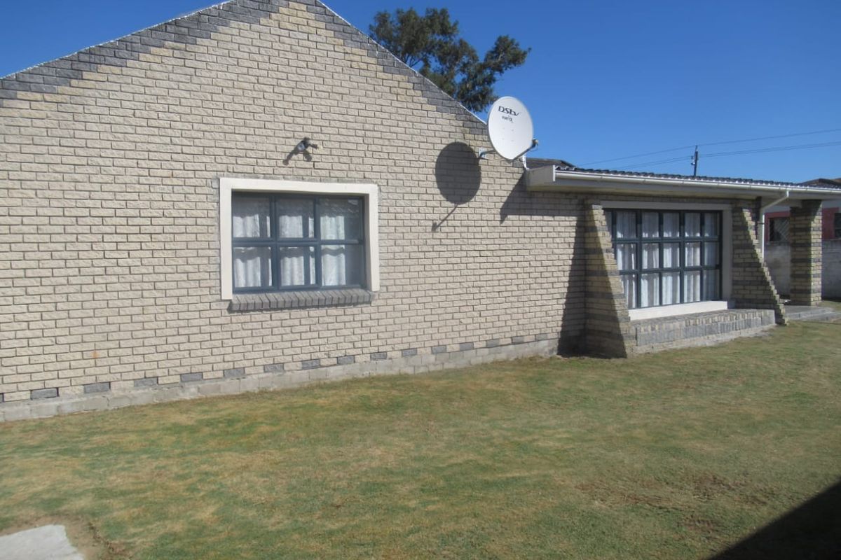 A view of the rear exterior of the house featuring face brick walls, aluminium window frames, and a well-maintained lawn area.