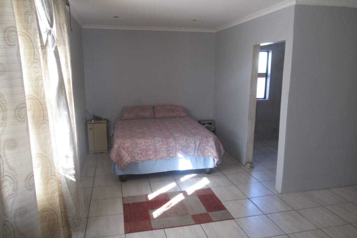 A functional bedroom featuring tiled flooring, recessed downlighting, and an adjoining space, offering a neutral canvas for potential interior updates.